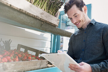 Poster - Smiling farmer's market worker checking inventory clipboard next to strawberries