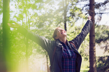 Canvas Print - Exuberant woman hiking smiling arms raised head back in sunny woods