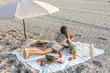Little girl eats fruit lying on a blanket on the beach.