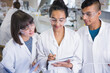 © KOTO - College students in lab coats discussing notes in science laboratory classroom