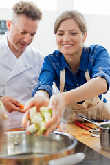 Woman placing food in pot in cooking class kitchen