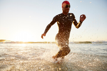 Wall Mural - Male triathlete swimmer in wet suit running from ocean