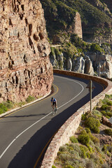 Wall Mural - Male triathlete cyclist cycling uphill along sunny cliffs