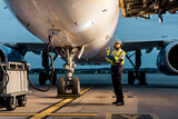 Fototapeta Miasto - Airport ground crew worker checking airplane on tarmac