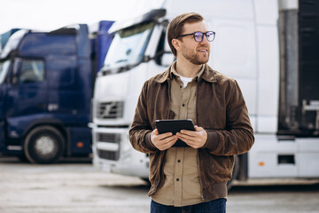 Truck driver standing by his lorry and using tablet