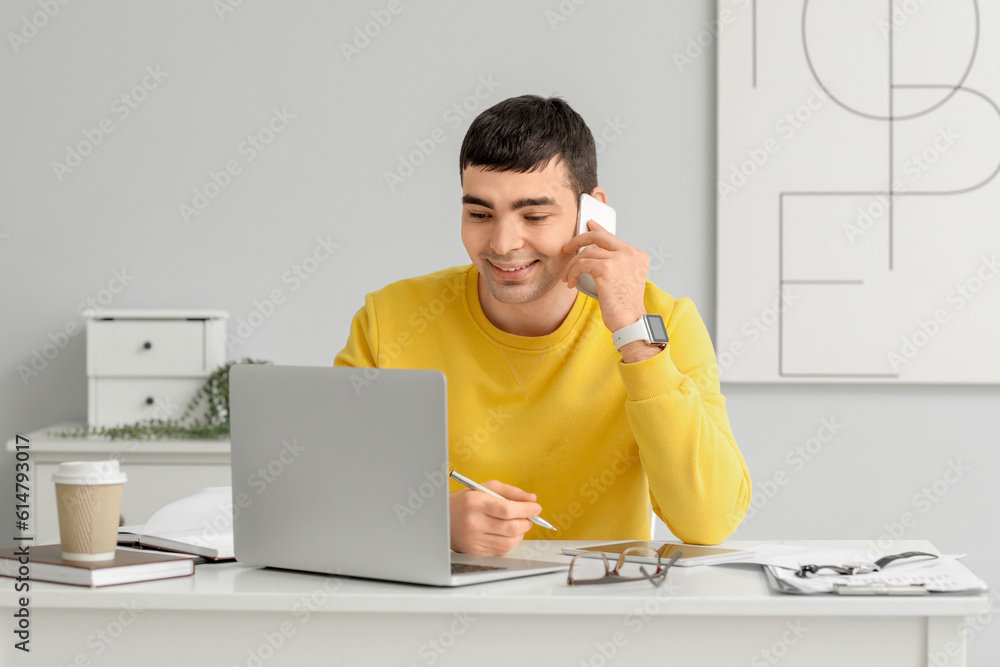 Young man talking by phone while sitting at workplace