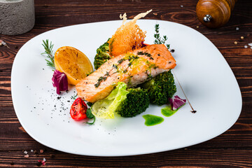 Wall Mural - Salmon steak with broccoli, tomatoes, lettuce and herbs in a plate.