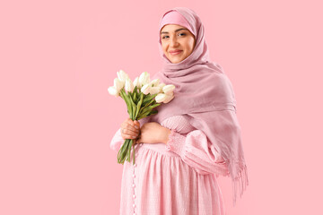 Wall Mural - Young pregnant Muslim woman with tulips on pink background