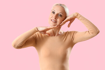 Poster - Mature woman doing face building exercise on pink background