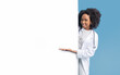 © Prostock-studio - Smiling young black curly lady doctor in white coat point hand to big banner with free space