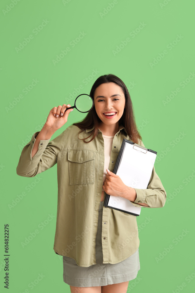 Young woman with magnifier and clipboard on green background