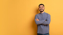 Confident Young Asian Man Standing With Folded Arms Over Yellow Background