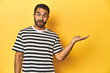 © Asier - Casual young Latino man against a vibrant yellow studio background, impressed holding copy space on palm.