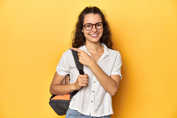 Wall Mural - Caucasian university student with glasses, backpack, smiling and pointing aside, showing something at blank space.