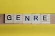 the word genre of gray small wooden letters lies on a yellow table