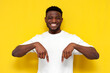 © Богдан Маліцький - joyful african american man in white t-shirt shows his hands down on yellow isolated background