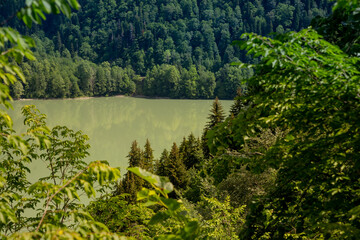 View through the trees on the lake between high and rocky mountains. Beautiful landscape.wild landscape.Scenic hiking views from Hill to green water lake