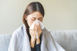 Sick, coronavirus or covid-19, attractive asian young woman, girl have a fever, flu and hand in use tissues paper sneezing nose, runny while sitting on sofa, couch at home. Health care on virus person