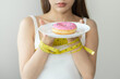 Diet, Dieting restrain asian young woman hand holding plate of donut, wrapped around arm with tape measure want to eat sugar doughnut, food of healthy when hungry. Weight loss person, temptation.