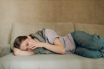 Young woman wearing scarf has flu ill sick disease cold at home indoor lying on sofa