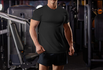 Wall Mural - Black t-shirt template on a posing athlete on the background of the gym, from head to knees, sportswear, front view.