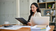 © bongkarn - An attractive Asian businesswoman is reading business reports at her desk in the office.