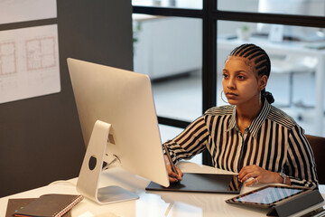 Aufkleber - Young African American webdesigner or artist with stylus drawing sketch on touchpad screen while sitting by workplace in front of computer