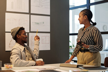 Aufkleber - Young confident architect pointing at blackboard with sketches of new buildings and looking at female colleague during presentation