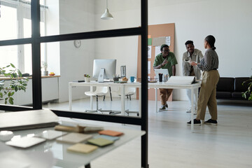 Aufkleber - Long shot of young African American designers in casualwear talking at meeting and discussing new creative ideas while standing by workplace