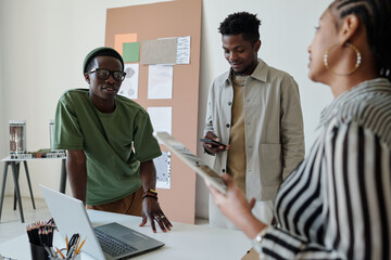 Aufkleber - Focus on two young businessmen standing by desk while one of them texting in smartphone and his colleague talking to female employee