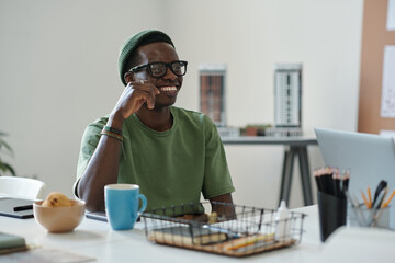 Aufkleber - Young cheerful African American male white collar worker in eyeglasses and casualwear sitting by workplace in office and looking at colleague