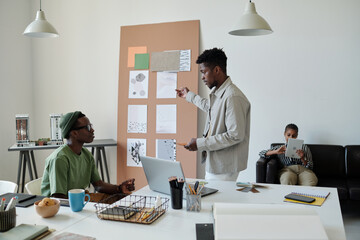 Aufkleber - Young confident architect in casualwear pointing at noticeboard with sketches on papers while talking to male colleague at meeting