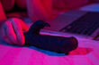 A woman lies in bed with a black dildo and looks at a laptop. Girl using sex toy in blue-red light. 