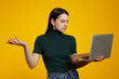 © Davidovici - Young caucasian woman with a laptop having doubts while raising a hand, isolated over yellow background.