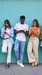 © CarlosBarquero - Group of multiracial teenagers online chatting and checking social media using phone technology addicted. They are isolated in blue wall outdoors standing in a row. Serious gen Z focus in mobile