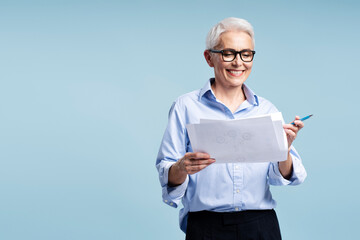 Wall Mural - Mature businessman wearing glasses holding business graph isolated on blue background, copy space