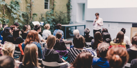 Wall Mural - female speaker giving presentation in lecture hall at university workshop. audience in the conferenc