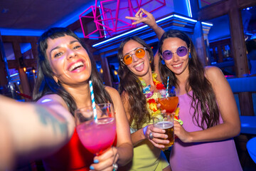 Smiling friends with glasses of alcohol in a nightclub taking a selfie at a night party