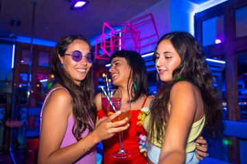 Fun of female friends in a nightclub dancing with the glasses at a summer night party in a pub