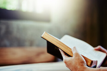 close up of a human hands hold while reading th open holy bible on wooden table with morning sunligh