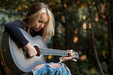 Music and hobbies. A talented young musician girl sits alone and composes songs on the guitar. The girl plays a calm melody on a musical instrument.