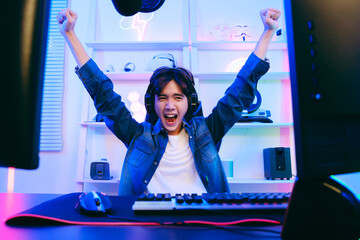 Portrait of Asian male gamer celebrating victory in front of the gaming table. Gamer winning an esports game with victory emotion. The player rejoices in victory in the competition.