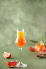 Wall Mural - Arancello in grappas wineglass, sweet Italian orange liqueur, traditional strong alcoholic drink and oranges on the green wooden background.