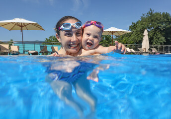 Wall Mural - Baby boy dives underwater in the pool with young mother