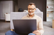 © contrastwerkstatt - An older man sits relaxed on the floor in the living room and looks at his laptop