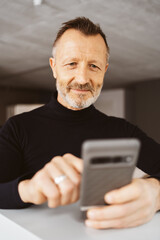 Wall Mural - 55-Year-Old Man with Turtleneck Looks Positively at His Smartphone