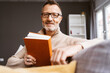 © contrastwerkstatt - bestager man with glasses sitting on sofa reading a book