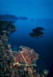 Amazing aerial panoramic view of the picturesque town of Dubrovnik with the old town, illuminated streets and buildings and marina with boats in blue hour after sunset.