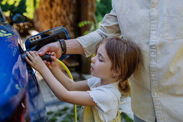 Wall Mural - Father with his little daughter charging their electric car.