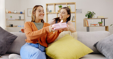 Wall Mural - Home, lesbians and couple with a surprise, gift and bonding in living room, happiness and relax. Partners, women and queer people in their lounge, present and celebrate relationship, marriage and wow